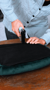 Persona utilizando una grapadora para reparar un cojín de silla sobre una mesa de madera.